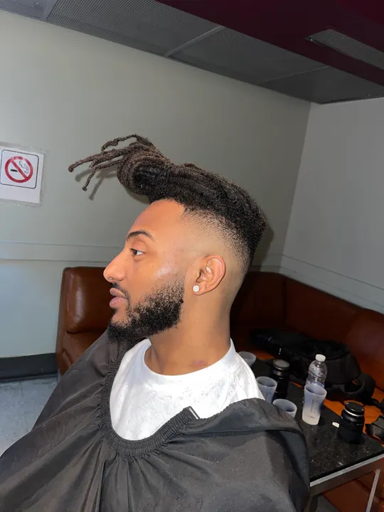 Locs tied up on top, with a fade and a beard, in the chair at the shop